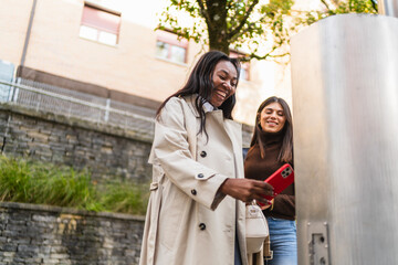 Happy women friends using a mobile phone to make a secure contactless payment at an outdoor terminal in the city