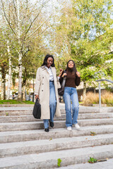 Obraz premium Two smiling women friends walking down outdoor concrete stairs in a park, enjoying conversation and casual time together