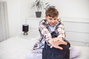 A teenage boy in a checkered shirt unpacks notebooks and school books from his backpack after...
