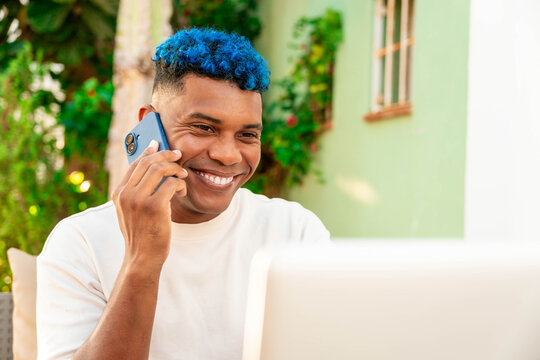 Smiling latin man talking on phone and working remotely on laptop outside. Embracing a modern lifestyle as a digital nomad - Powered by Adobe
