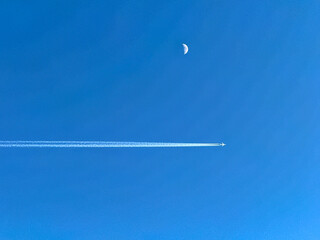 Holiday jet in flight with contrails passing the moon on a deep blue sky