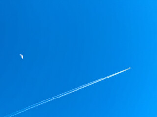 Holiday jet in flight with twin contrails passing the moon on a deep blue sky