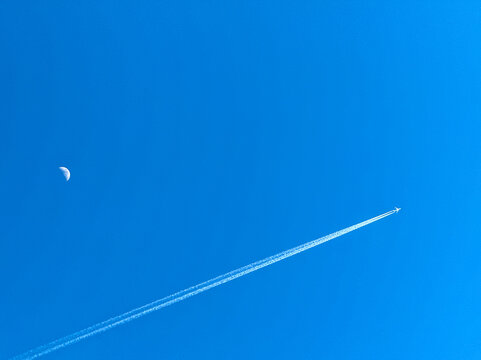 Holiday jet in flight with twin contrails passing the moon on a deep blue sky - Powered by Adobe
