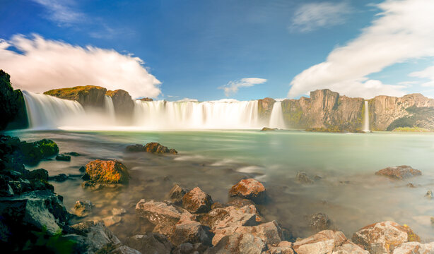 View of cascading waterfalls spill into a tranquil pool, framed by rugged cliffs under a bright sky, creating a serene scene, Fossholl, Pingeyjarsveit, Iceland.