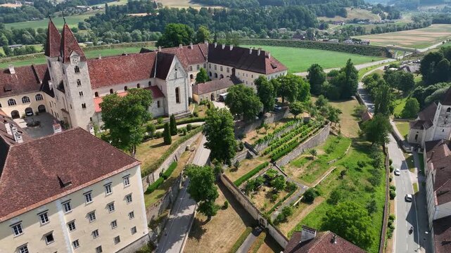 Aerial summer scenery of Sankt Paul im Lavanttal with monastery complex, rooftops, valley landscape, green hills, calm cinematic drone movement, warm atmospheric tones