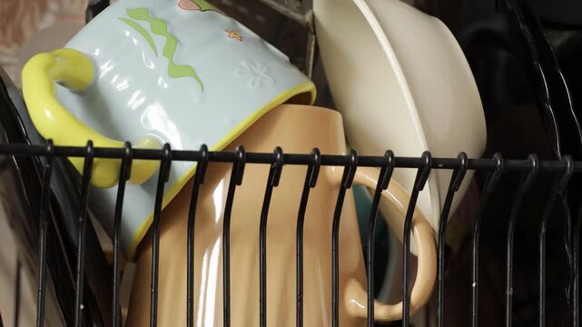 A black wire basket filled with various dishes and cups, perfect for displaying kitchenware