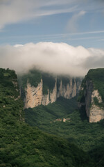 Majestic green valley with towering rock cliffs partially shrouded in dramatic clouds under a blue sky