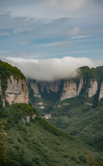 Majestic green valley with towering rock cliffs partially obscured by lowhanging clouds