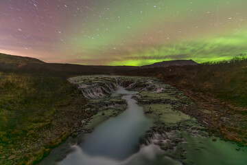 View of the Bruarfoss Waterfall's turquoise waters cascading through rugged lava rocks under the mesmerizing dance of the aurora borealis, Blaskogabyggo, Blaskogabyggo, Iceland.