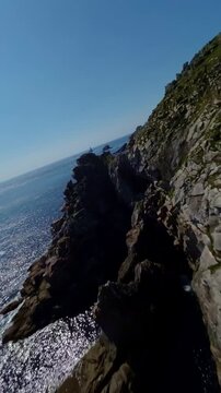 FPV drone flies over green slopes and rugged cliffs at Pointe du Raz with open ocean views