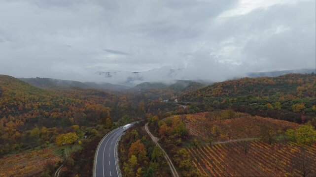 A dramatic drone shot capturing a truck moving along the national road to Prilep on a rainy autumn day with wet asphalt, mist, and atmospheric weather.