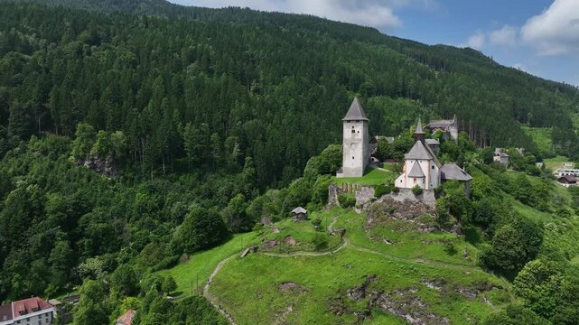 Summer drone footage showing medieval Friesach, old fortified walls, rooftops, towers, hills, serene atmosphere, warm daylight, gentle cinematic motion