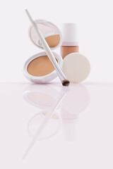 Compact powder and foundation in pump bottle, makeup brush and puff on glossy surface