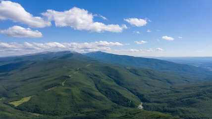 Panoramic aerial view of lush green mountain ranges under a clear blue sky with white clouds