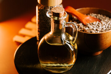 Sunflower oil in a glass bottle next to seeds and wooden bowl on a dark table