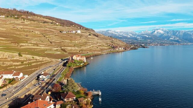 Aerial view of Glerolles Castle nestled on the shores of the lake, contrasting against the terraced vineyards and snow-capped mountains, Saint-Saphorin, Vaud, Switzerland.