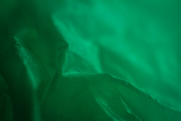 Extreme close up of green empty plastic bag background. The plastic surface is wrinkly and tattered making abstract pattern. Selective focus, shallow depth of field.