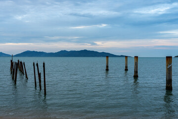 Old wooden pier pilings in the sea with a mountain backdrop at dusk