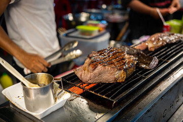 Grilled steak cooking on a hot grill at a street food market