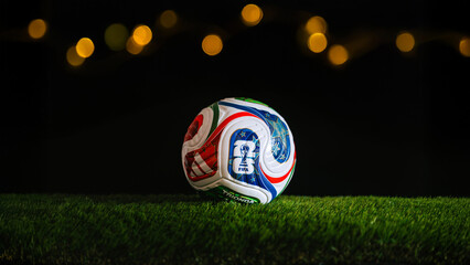 Fototapeta premium FIFA World Cup 2026 backdrop featuring warm stadium bokeh and dark edit space for text. Panorama format 16:9, official Trionda ball on green grass