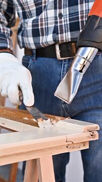 Carpenter using heat gun and wood scraper removes paint from old wooden window. Construction industry, carpentry. Restoration. Footage.