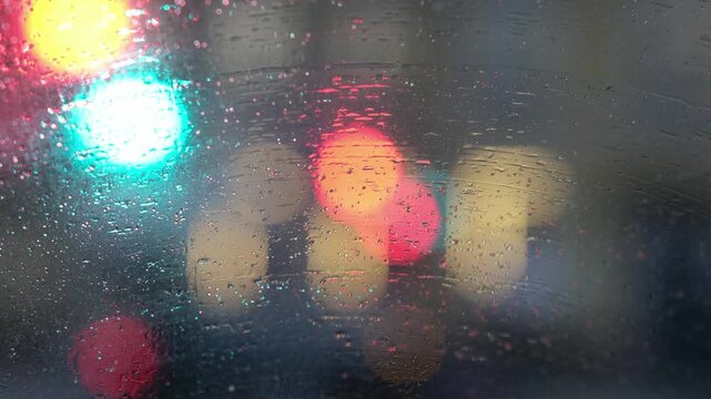 Extreme close-up of rain drops on a car window at night. Bright city lights and neon signs create a beautiful bokeh background. Moody, cinematic atmosphere for introspective and urban storytelling