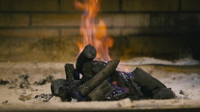 Slow-motion dolly shot of burning charcoal with rising flames, capturing the heat and glowing embers used for a barbecue or fireplace in a warm, rustic setting. High quality FullHD footage