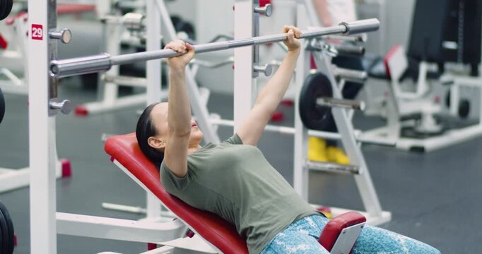 Gym workout. Middle aged Caucasian woman trains her pectoral muscles in the gym. 4k footage of a Caucasian woman trains chest muscles using bench press during gym workout.