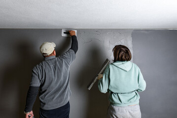 Workers applying and smoothing decorative pebble plaster using a putty knife and float on a wall.