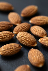 Whole almonds scattered on dark background crisp close up