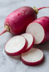 Whole and sliced radishes on wet marble surface macro shot