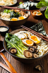 Traditional ramen with jerked pork or chicken.  With udon or ramen noodles. Served in classic bowls. Gyoza dumplings and mushrooms in the background.