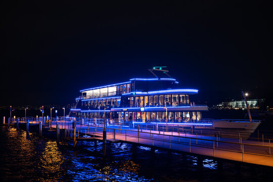 Zurich HB, Switzerland, December 5 2025. Panta Rhei passenger cruise ship docked on lake Zurich at night, Beautiful blue lights reflected in the water, people having dinner aboard the vessel