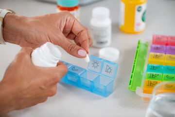 Medicine adherence. Filling pills into a weekly organizer to structure her medication routine. Highlights precise sorting, dose planning, and responsible health management.
