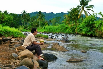 A man takes a refreshing sip of young coconut water, highlighting natural hydration in a tropical outdoor atmosphere.