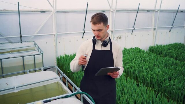 Modern agricultural technology. Dutch farmer uses special device to measure acidity of water in plant watering tank, records data on tablet for crop growth monitoring. Biotechnology for growing flower