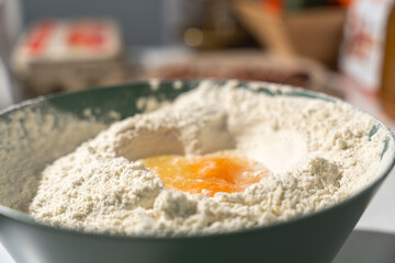 Raw egg cracked into a flour well in a mixing bowl, ready for homemade dough. Baking ingredients in a warm kitchen close-up.