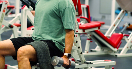 Gym workout. Cropped view of a young Caucasian man trains his bicep muscles with dumbbells in the gym. Man trains bicep muscles with controlled movements, emphasizing strength and endurance in gym.