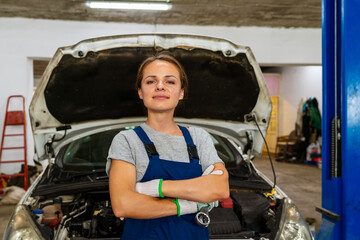 Confident female car mechanic with crossed arms in local car repair shop. Woman at work conceptual photo.