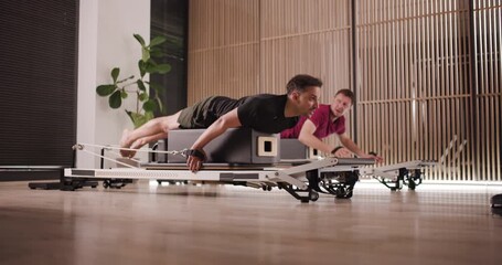 Participants perform various strength exercises in a stylish fitness studio featuring light wood decor and state-of-the-art reformer machines. Motivation fills the air as they challenge themselves - Powered by Adobe