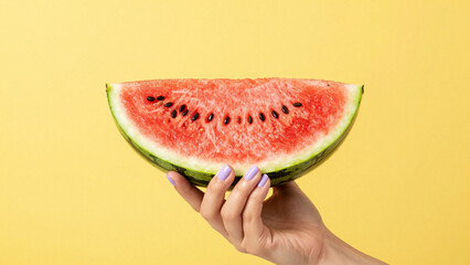 A vibrant slice of fresh watermelon held by a hand against a clean yellow background