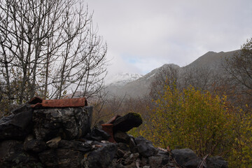 Cascading Rain Over Serene Mountain Peaks, Cantabria - Serene mountain landscape features a stone wall amidst green vegetation, snow-capped peak, and grey-brown terrain in La Hermida-Bejes, Cantabria