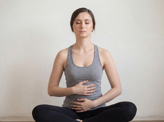 A woman sits on the floor in a simple room, performing yoga by focusing on her breath