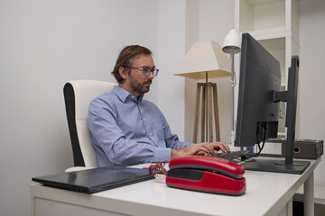 A businessman types on a computer keyboard at a modern desk while working in a clean office environment.