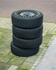 four black car tires lie stacked on top of each other outside on the sidewalk