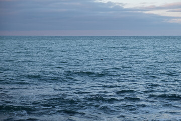 Atmospheric seascape. Blue clouds bright rays of the sun illuminate the smooth surface of the sea, ocean. Panoramic view with a lighthouse on the horizon. The concept of peace, tranquility, relaxation