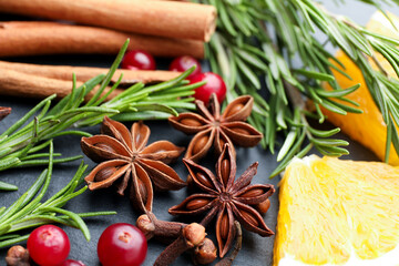 Different spices, fresh rosemary, cranberries and orange slice for mulled wine on black table, closeup