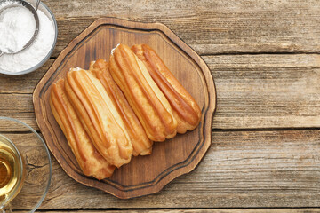 Tasty eclairs, powdered sugar and tea on wooden table, flat lay. Space for text