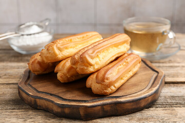 Tasty eclairs, powdered sugar and tea on wooden table, closeup