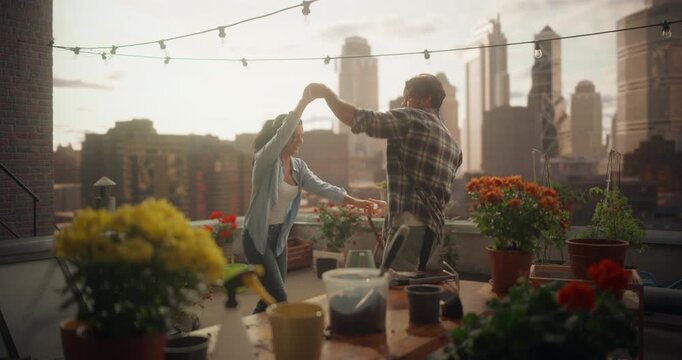 Couple Joyfully Dance and Spin Together Between Potted Plants, Laughing and Improvising Playful Steps While Taking a Break From Gardening on a Cozy Rooftop Patio with City Skyline in the Background.